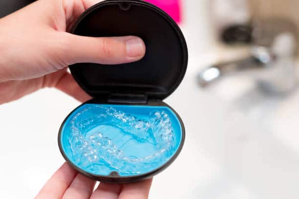 Smiling adult holding Invisalign clear aligner case